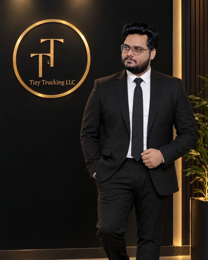 Muhammad Ali, CEO of Tizy Trucking LLC, standing in front of the company logo wall